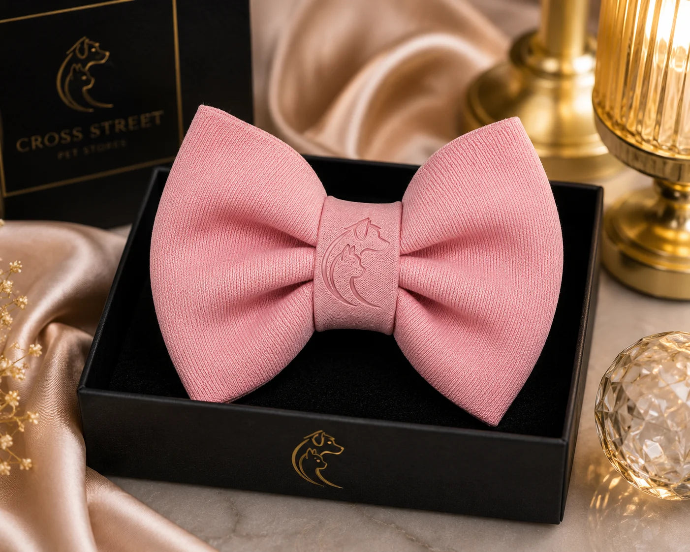 Pink bow tie with embossed dog logo in black gift box on marble table with gold decor