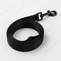 A black nylon dog leash with a metal clip and logo on a white marble background