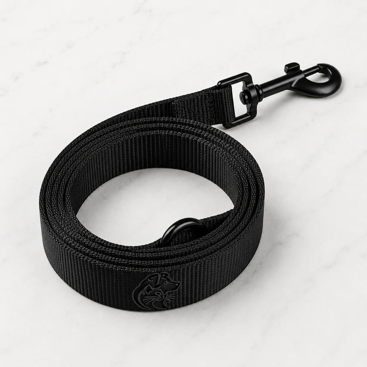 A black nylon dog leash with a metal clip and logo on a white marble background