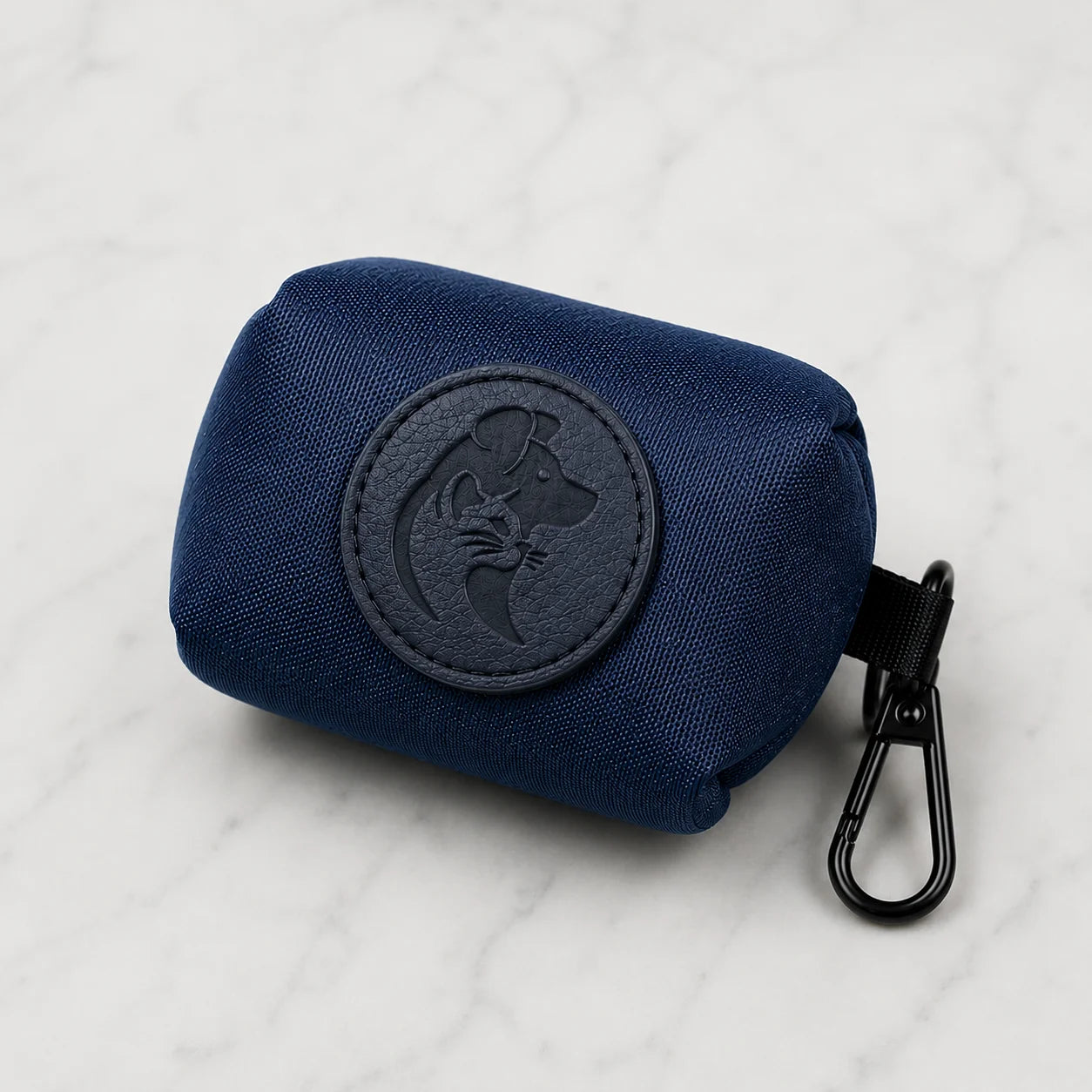 A navy blue fabric pouch with a dog logo and black carabiner on a marble surface