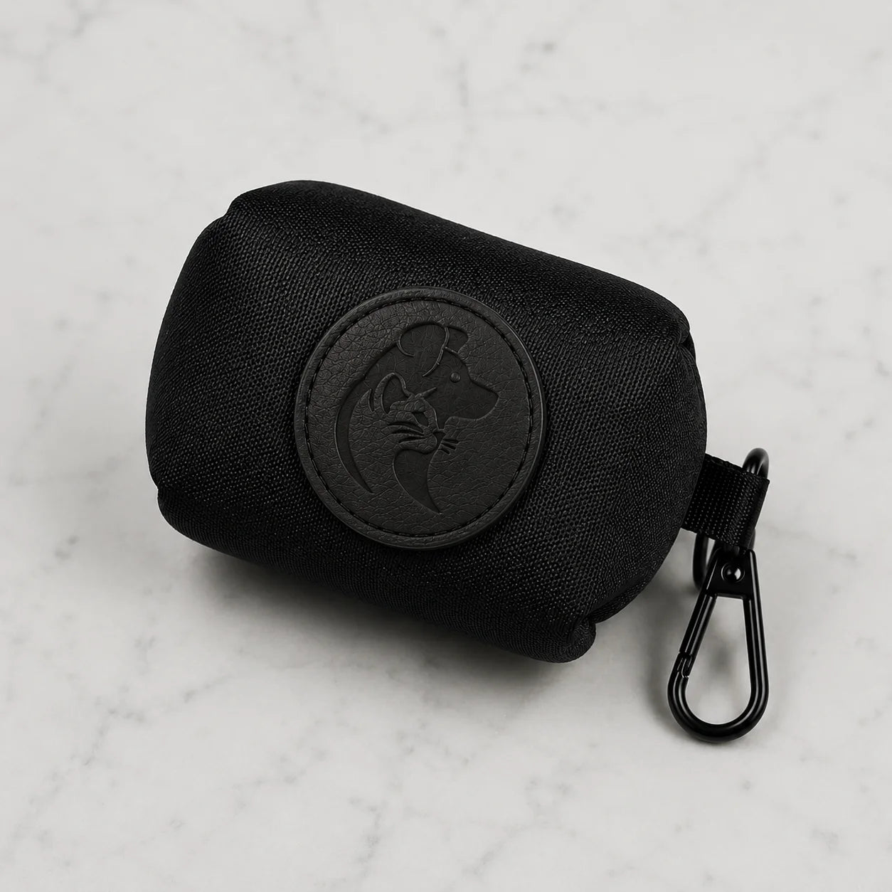 Black dog poop bag holder with metal clip and embossed dog logo on white marble background