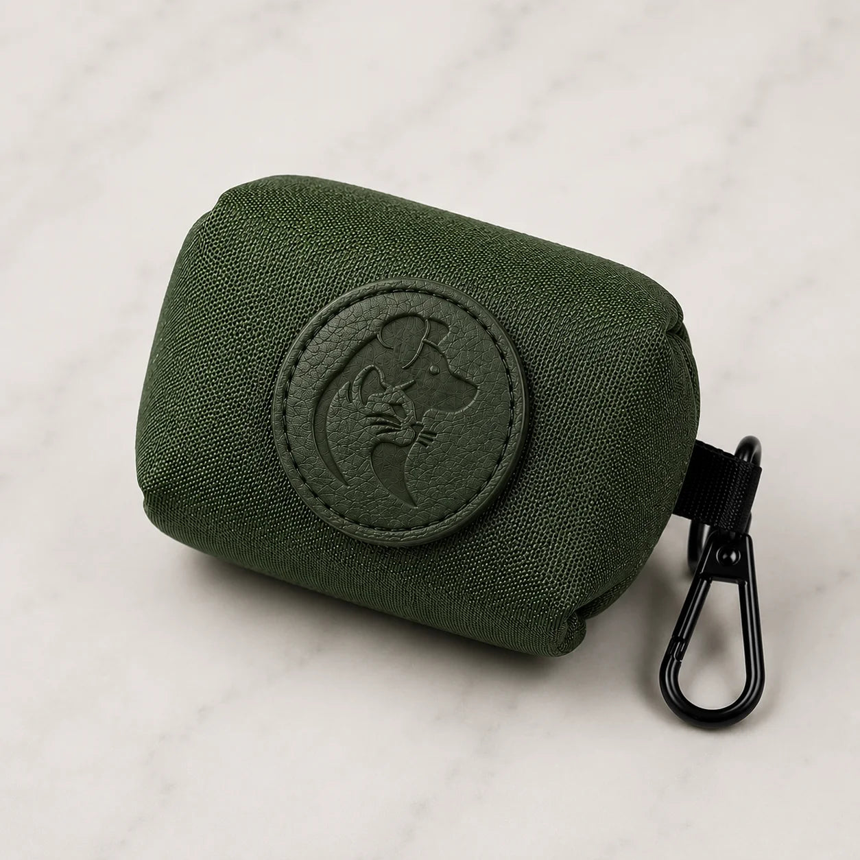 Green fabric dog poop bag holder with black clip and embossed dog logo on white marble background