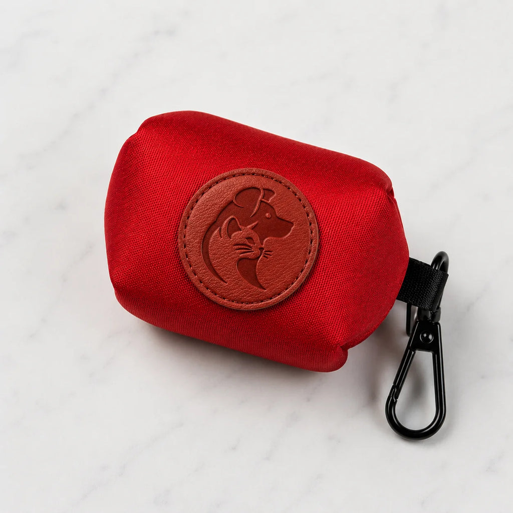 Red dog poop bag holder with black clip and brown logo on white marble surface