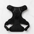 Black dog harness with adjustable straps and buckles on a white marble background