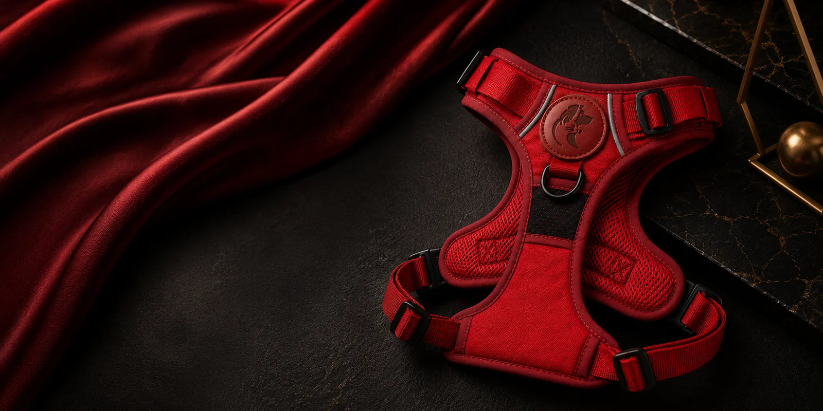 Red dog harness on black background with draped fabric and gold accents nearby