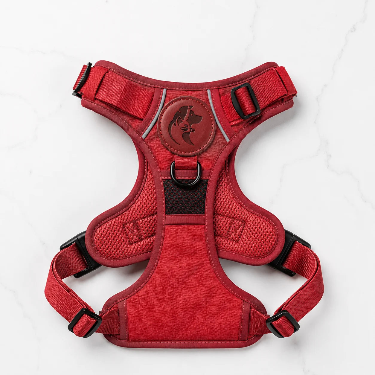Red dog harness with adjustable straps and logo on white marble background